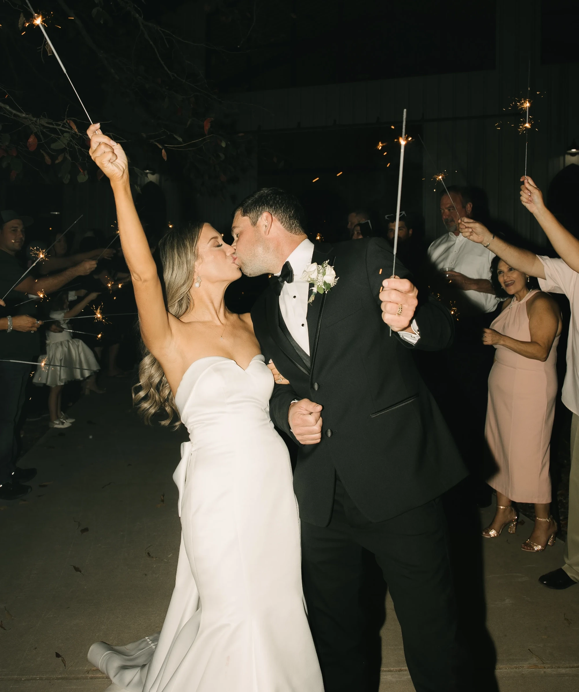 Photo of a bride and a groom kissing while holding a sparkling torches.
